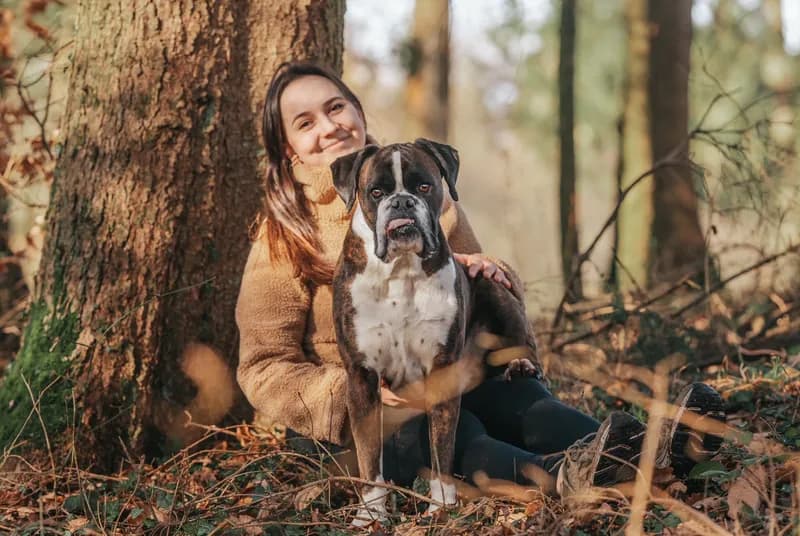 Lena Heintz sitzt mit einem Boxer an einem Baum im Wald